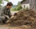 Člověk dřepí vedle hromady tmavého chlévského hnoje se slámou a prohlíží si hrst materiálu.